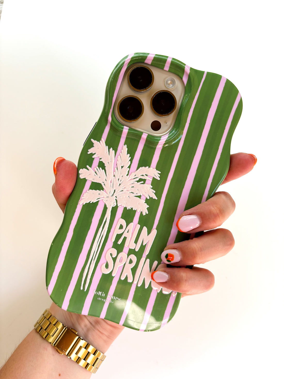 Green phone case with pink stripes and palm tree design held by a hand.