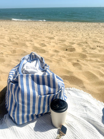 Blue and white striped beach bag and coffee cup on a beach with ocean view